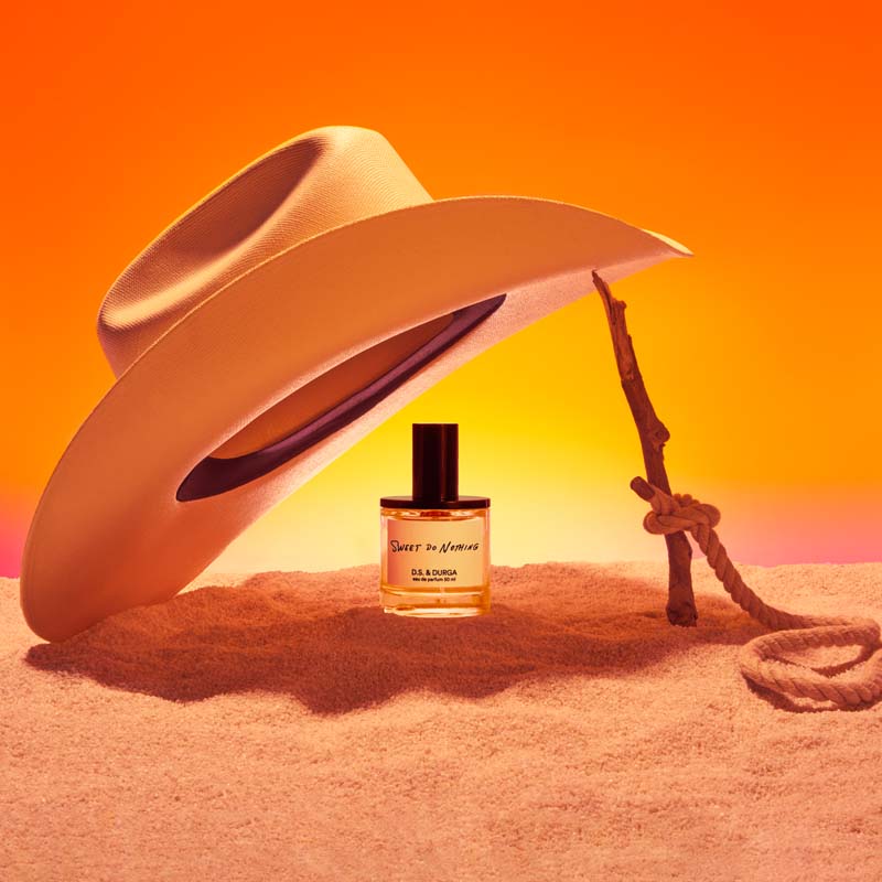 D.S. &amp; Durga Sweet Do Nothing Eau de Parfum showing bottle underneath cowboy hat on sand