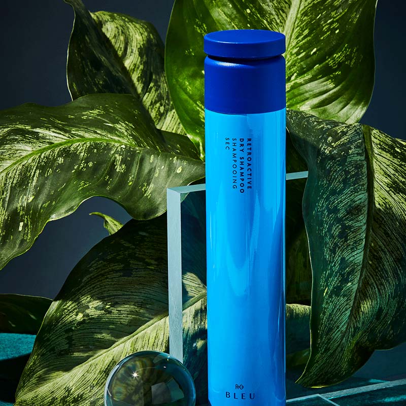 R+Co Bleu Retroactive Dry Shampoo showing product sitting in front of plant