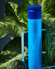 R+Co Bleu Retroactive Dry Shampoo showing product sitting in front of plant