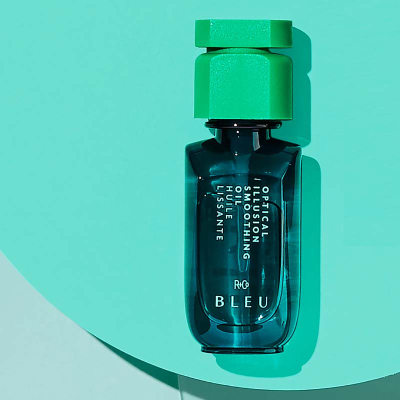 R+Co Bleu Optical Illusion Smoothing Oil showing sitting on a blue background