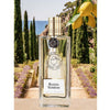 Parfums de Nicolai Riviera Verbena Eau de Toilette sitting next to lemons and a beautiful backdrop of green trees and ocean