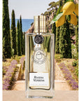 Parfums de Nicolai Riviera Verbena Eau de Toilette sitting next to lemons and a beautiful backdrop of green trees and ocean