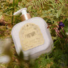 Santa Maria Novella Fresia Fluid Body Cream sitting on green bushes and grass