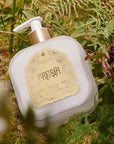 Santa Maria Novella Fresia Fluid Body Cream sitting on green bushes and grass
