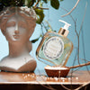 Santa Maria Novella Angeli di Firenze Liquid Soap sitting in a bowl of salt rocks with a stone head vase 