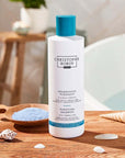 Christophe Robin Purifying Shampoo with Thermal Mud showing on counter surrounded by sea shells 
