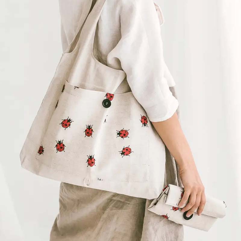 Sava Seasons Foldable Linen Shopper Tote – Ladybugs showing tote on shoulder and one tote folded in hand