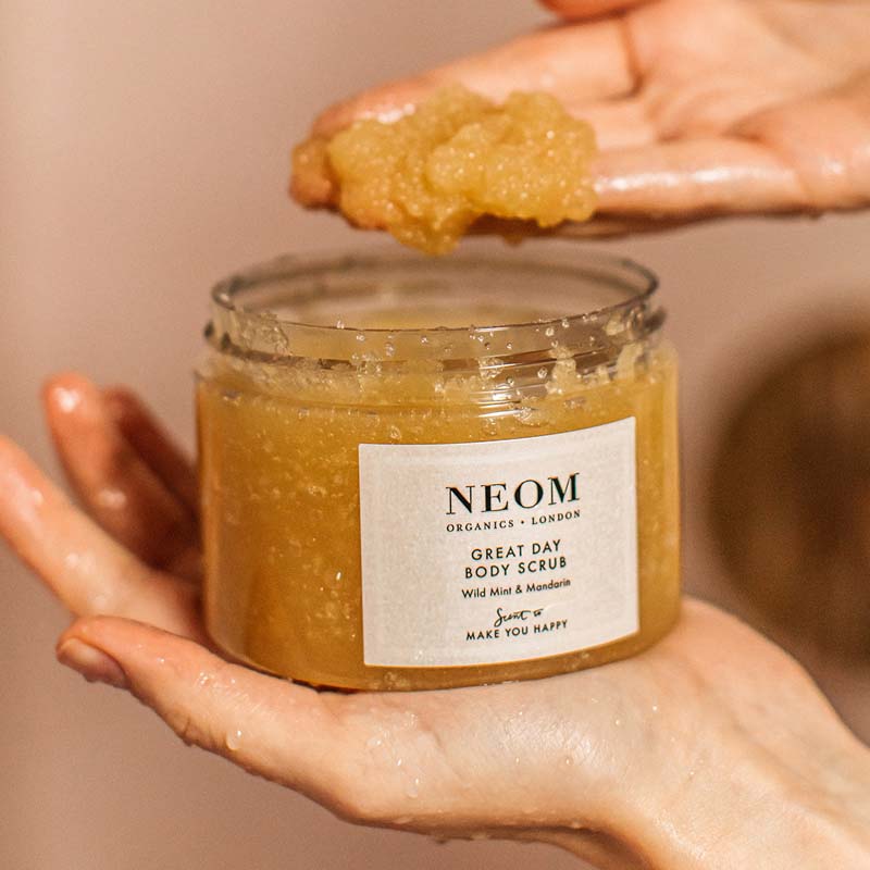Lifestyle shot of Neom Organics Great Day Body Scrub with model scooping out with hand scrub