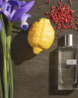 Chantecaille Vetyver Cedre Eau de Parfum surrounded by purple flowers, lemon and pomegranate seeds