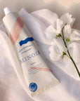 Minois Paris Soin Demelant Hydratant (Moisturizing Detangling Conditioner) showing on white fabric next to a white flower