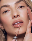 Model applying Close up of Roen Beauty Kiss My Liquid Lip Balm - Lola on lips