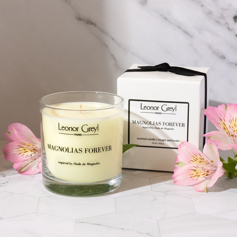 Lifestyle shot of Leonor Greyl Magnolias Forever Candle (11 oz) with box and pink flowers in the foreground and background