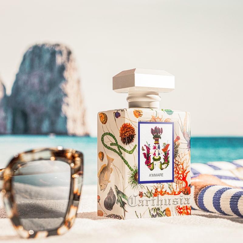Carthusia A’mmare Eau de Parfum sitting on towel with sunglasses and ocean in the background