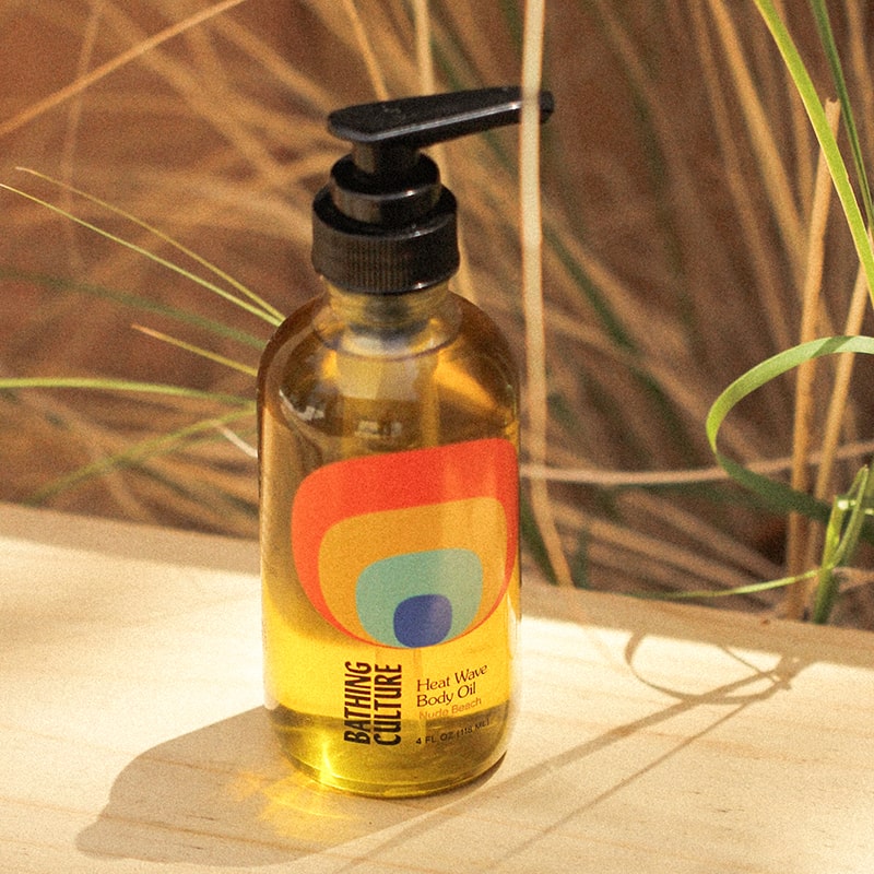 Bathing Culture Heat Wave Body Oil - Nude Beach (4 oz) showing on a piece of wood with plants behind it