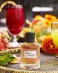 The Maker Paradiso Eau de Parfum (50 ml) sitting on a  tray with tropical looking drinks and fruit in the background