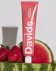 Davids Premium Toothpaste - Kids + Adults Strawberry Watermelon shown sitting on a watermelon next to strawberries