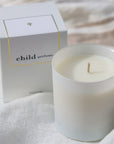 Lifestyle shot of Child Perfume Scented Candle 8 oz shown with box sitting on white linen fabric