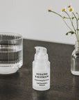 Susanne Kaufmann Rejuvenating Eye Cream lifestyle shot of product on wood table with a glass of water and a small vase with flowers in it