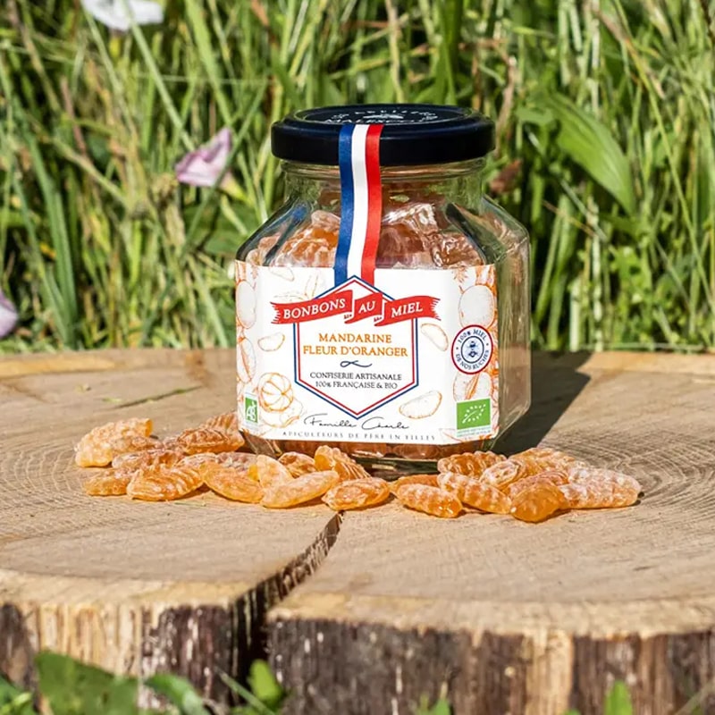 Les Abeilles de Malescot Tangerine &amp; Orange Blossom Honey Candies beauty shot of jar on tree stump with candies in front of jar