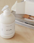 Tangent GC Fir Body Lotion - Product displayed on table next to magazine