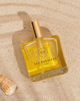 LES PANACEES Nourishing Dry Body and Hair Oil - Summer Tourbillon - Product displayed on beach sand