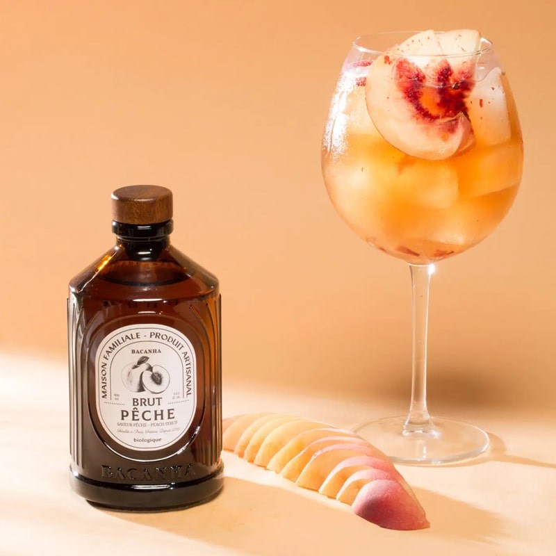 Bacanha Organic Raw Peach Syrup - Product shown next to wine glass with peach drink.