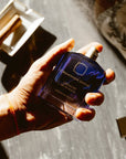Ormonde Jayne Verano Eau de Parfum - model hand holding perfume bottle, cigar on tray in background