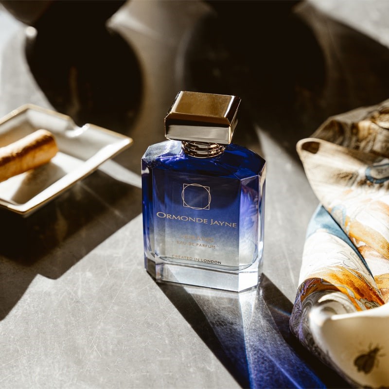 Ormonde Jayne Verano Eau de Parfum - perfume bottle next to cigar on tray and cloth on stone table