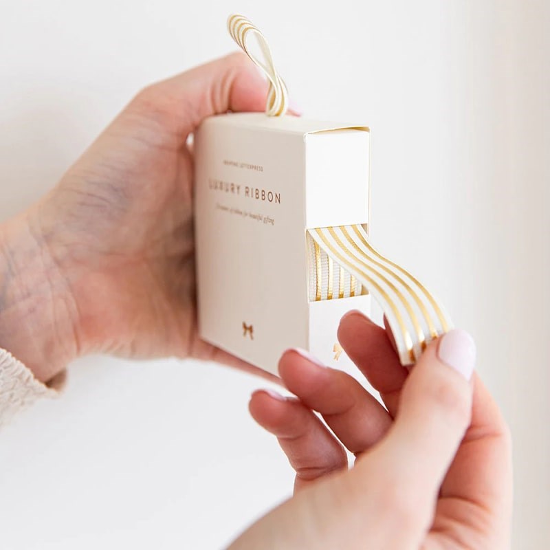 Bespoke Letterpress Cream Gold Foil Striped Ribbon - Model shown holding ribbon box and pulling ribbon out
